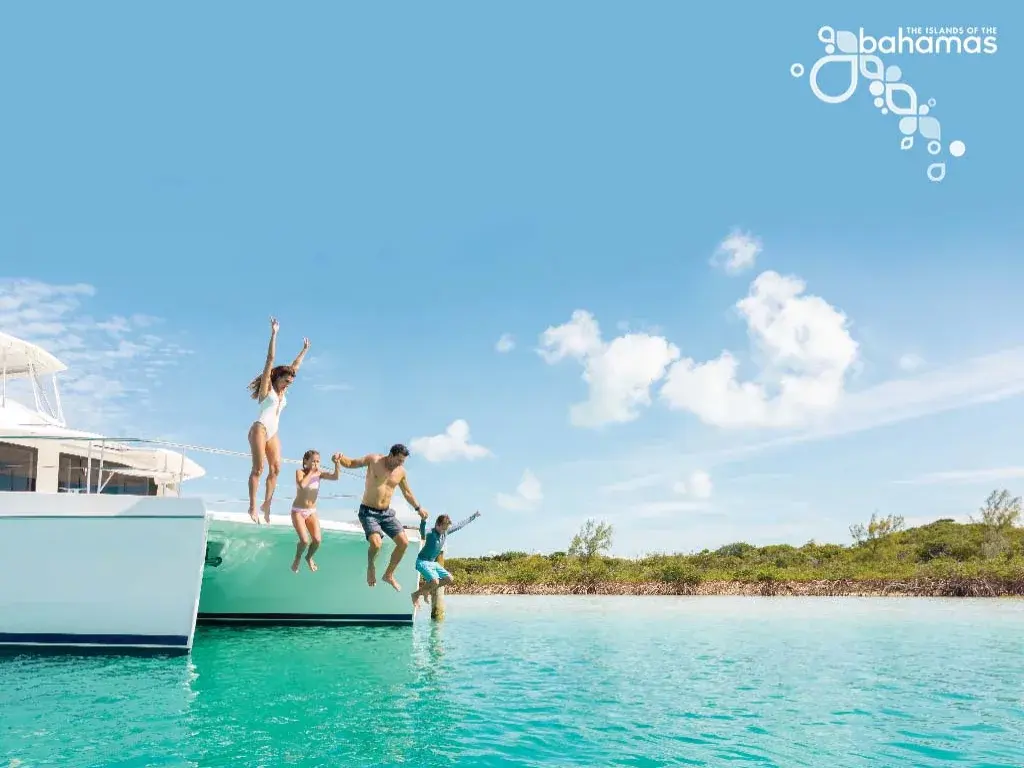Four travelers jump off a catamaran into clear shallow water.