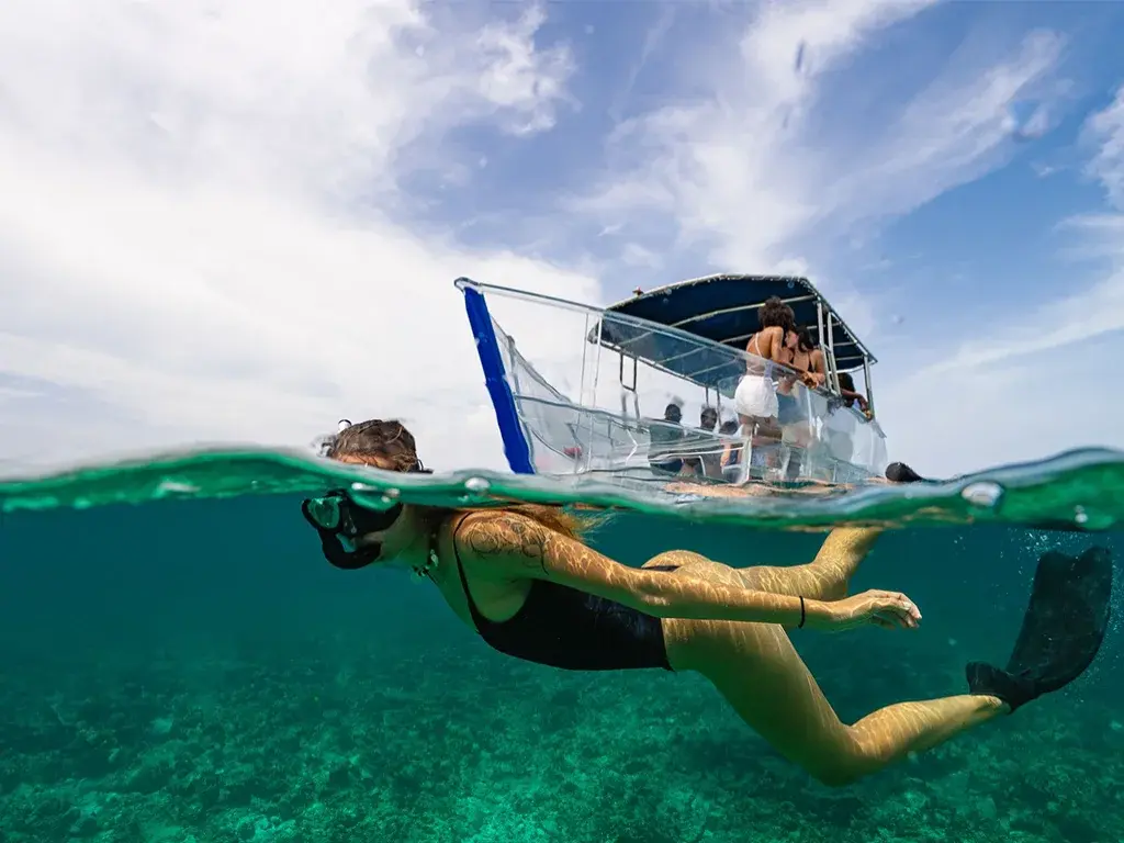 A snorkeler swims through clear water beside a small boat.