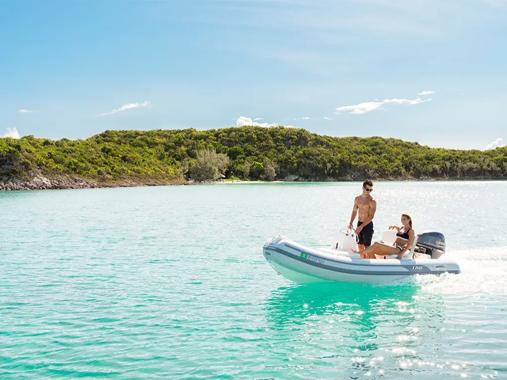 A couple in an inflatable boat floats in pale-turquoise shallows of the Berry Islands.