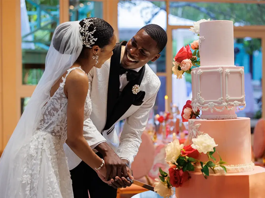 Newlyweds cut a pink wedding cake.