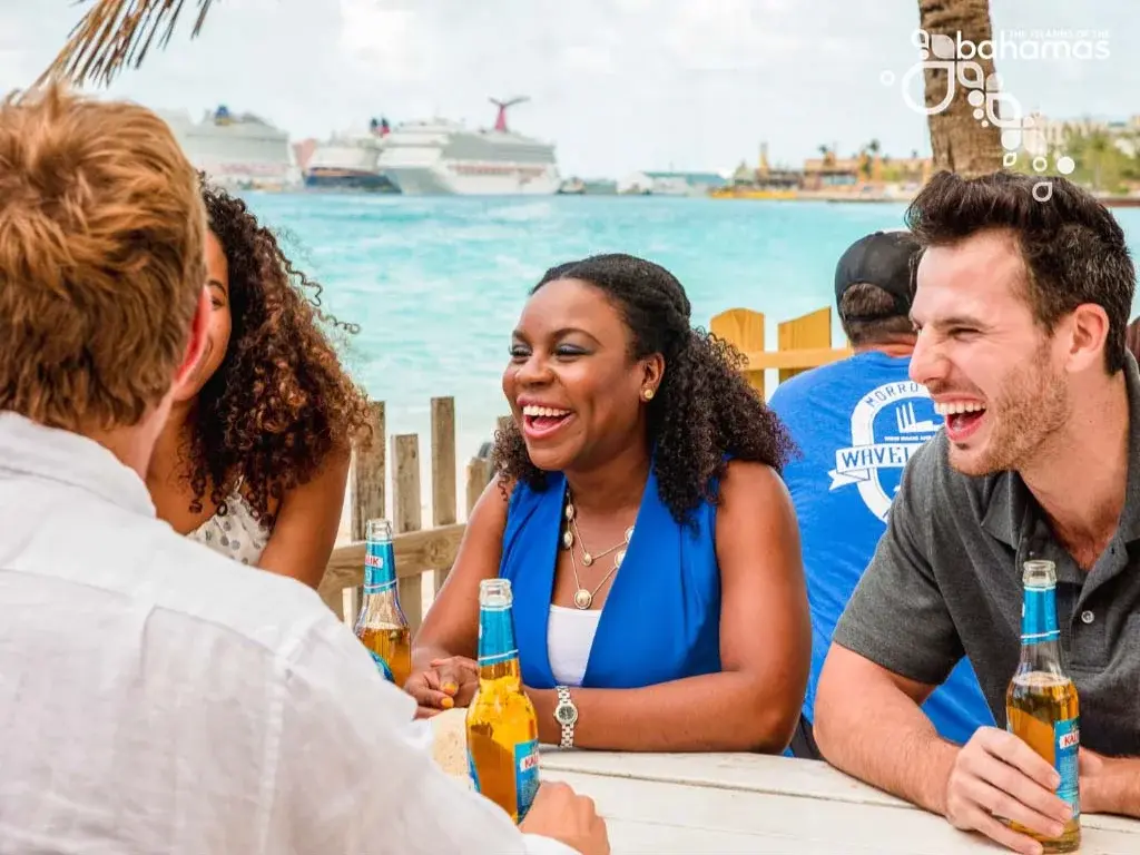 Friends share drinks at a waterfront bar, with a cruise ship behind them.