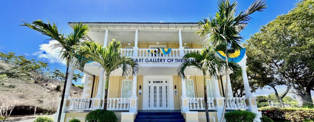 A wide view of the yellow and white colonial villa of the National Art Gallery, among palms.